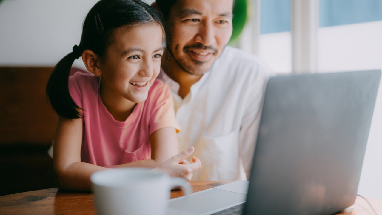 Father and young daughter on video call on laptop at home