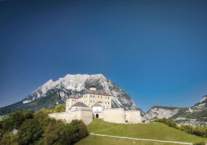 Ansicht auf Schloss Trautenfels bei blauem Himmel, im Hintergrund ist ein Berg zu sehen.