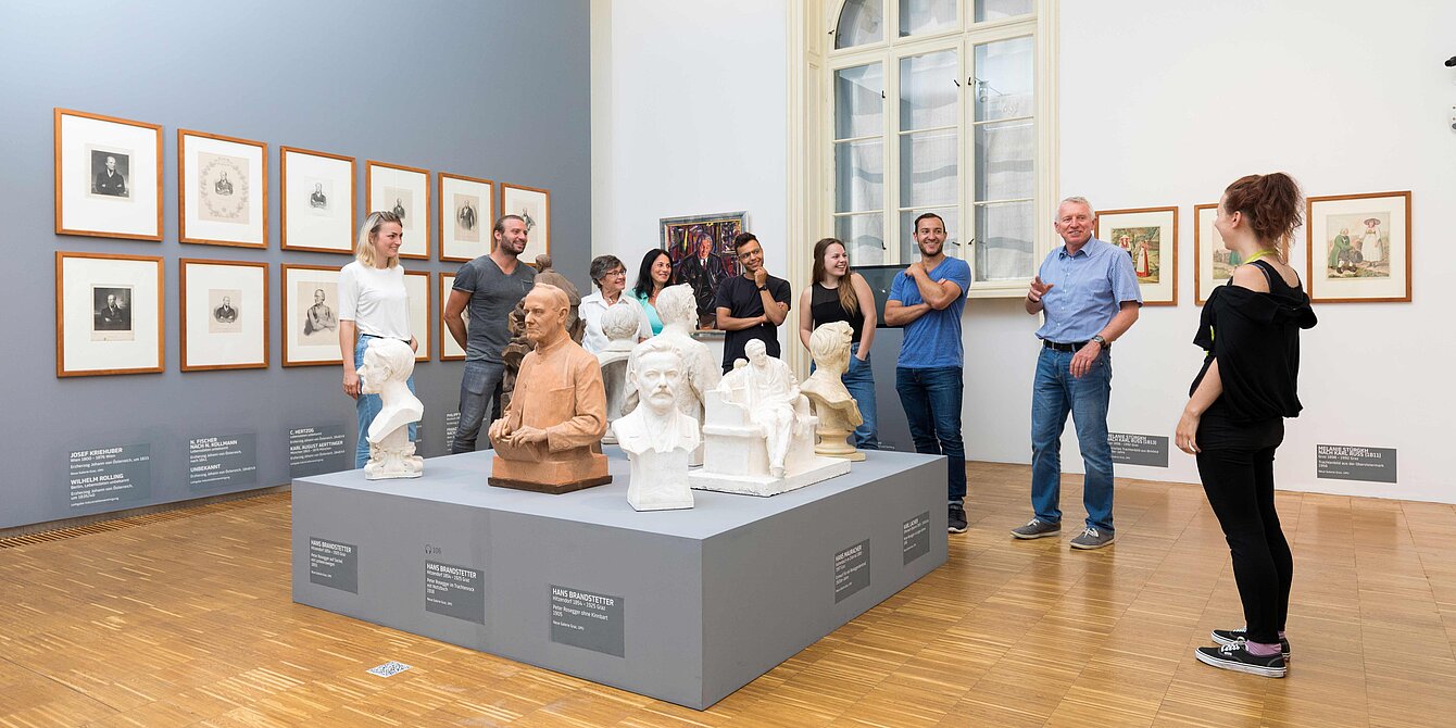 Eine Museumsmitarbeiterin führt eine Gruppe an Besucher:innen durch eine Ausstellung in der Neuen Galerie Graz.