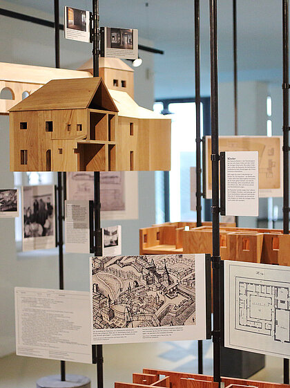 Dekoratives Ausstellungselement zur Geschichte des Volkskundemuseums am Paulustor mit alten Gebäudeplänen und Miniaturmodellen aus Holz.