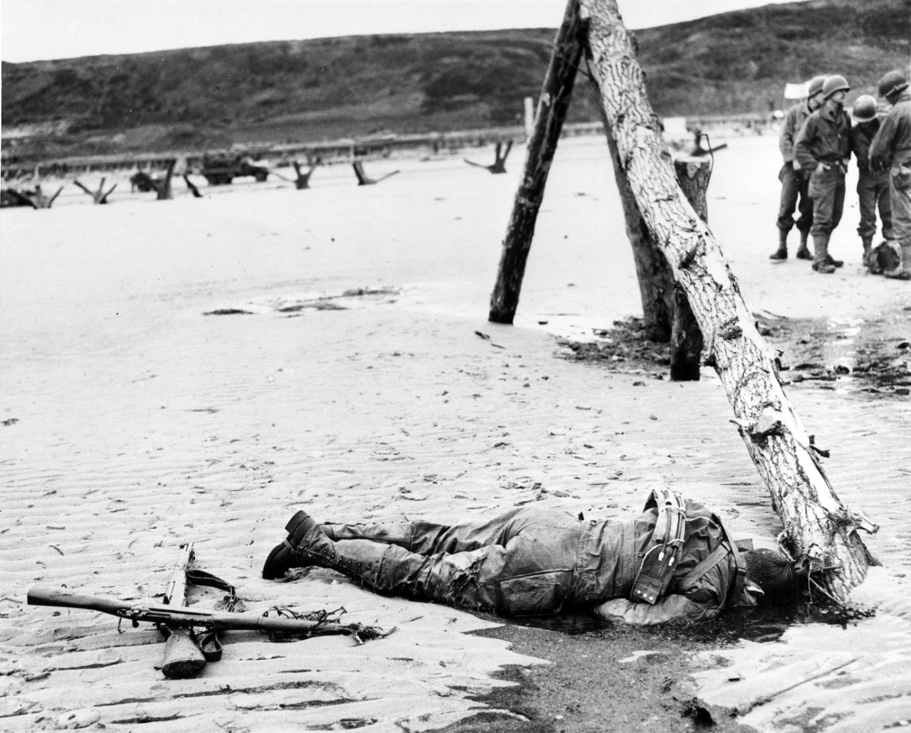 An American Soldier lies dead alongside an anti-landing craft obstruction on Omaha Beach