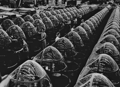 Factory with rows of airplane noses being inspected by women during WWII