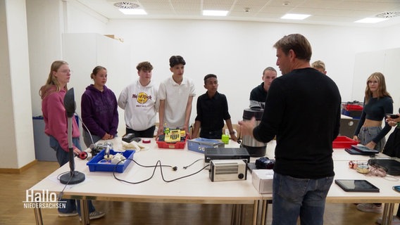 Schülerinnen und Schüler stehen rund um einen Tisch, auf dem verschiedene Elektrogeräte stehen. © Screenshot 