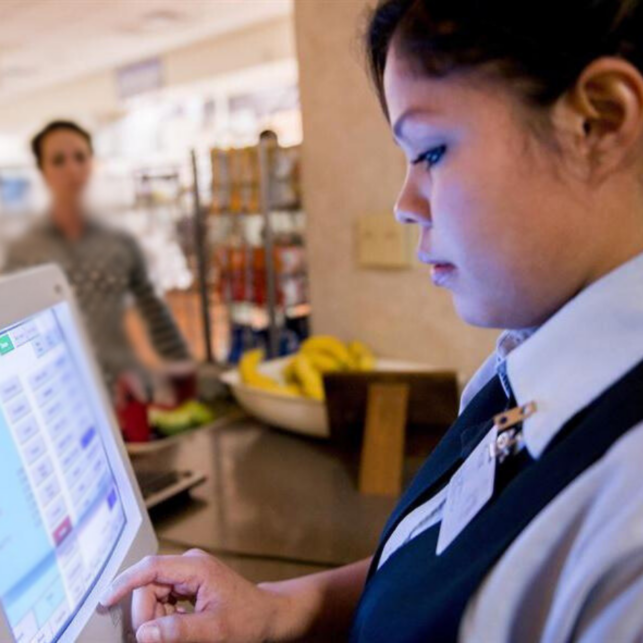 A cashier wearing a vest and nametag uses a point of sale system