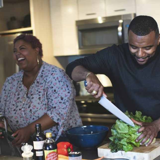 A smiling Black man and woman prepare a meal together in their home kitchen