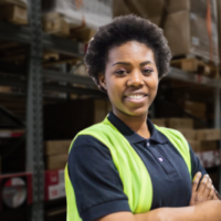 A warehouse worker folds her arms in front of a background of stacked pallets