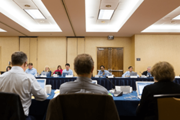 Panel of reviewers with laptops in a conference room.