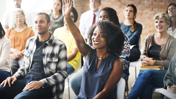 group of smiling people in meeting raising their hands