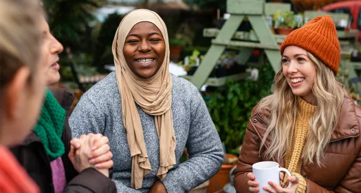 Group of warm clothed women, seated outside, smiling and laughing