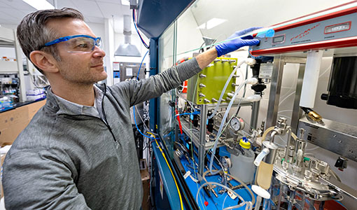 a researcher with safety glasses and a lab coat working on equipment in a lab