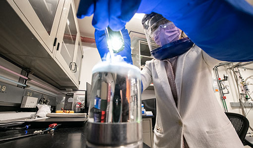 One researcher with safety glasses and a face mask working on equipment in a lab.