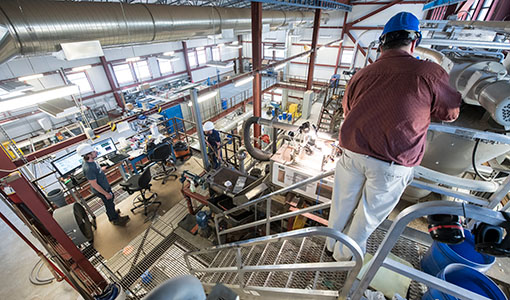 One researcher in a hard hat working on equipment in a lab.