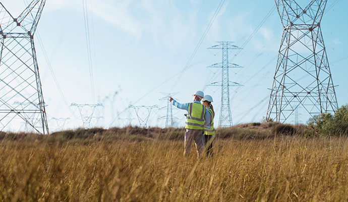 Two people stand in a field pointing at power transmission lines