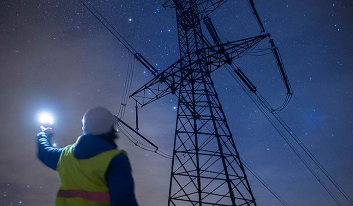 Person holding flashlight looking up at transmission power pole in the dark