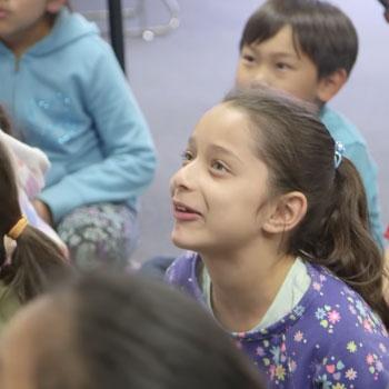 Group of young students on floor of classroom listening to teacher