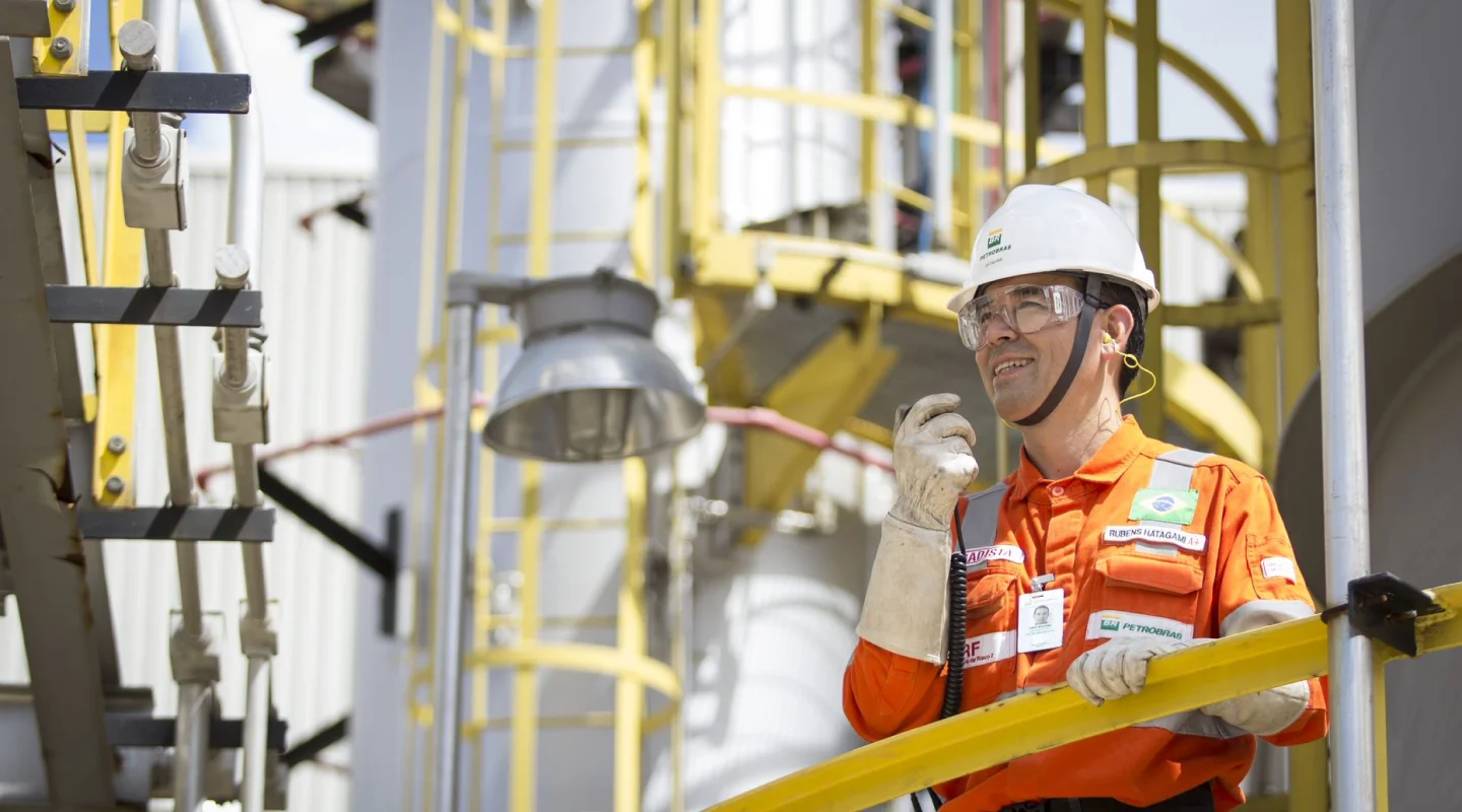 Funcionário da Petrobras falando a um walkie talkie, utilizando equipamento de proteção completo.