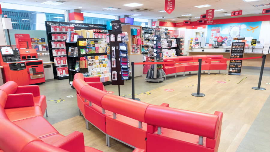 Wide shot of an empty Post Office branch with seats, queue system, shelves and counter in view