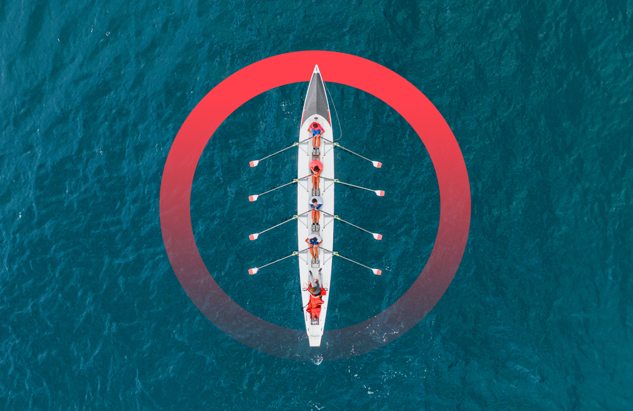 A bird's-eye view of a five-person rowing team in a racing row boat surrounded by water.