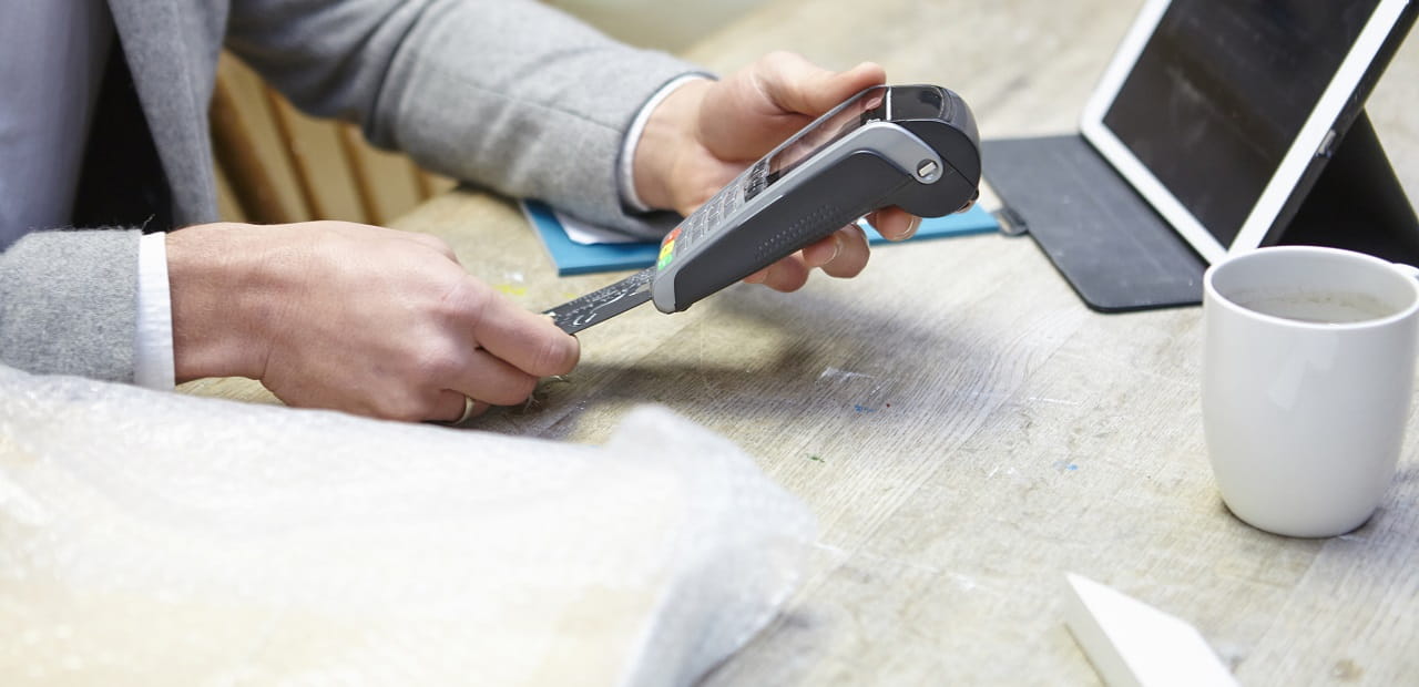 Male hands use a credit card scanner at a retail counter.