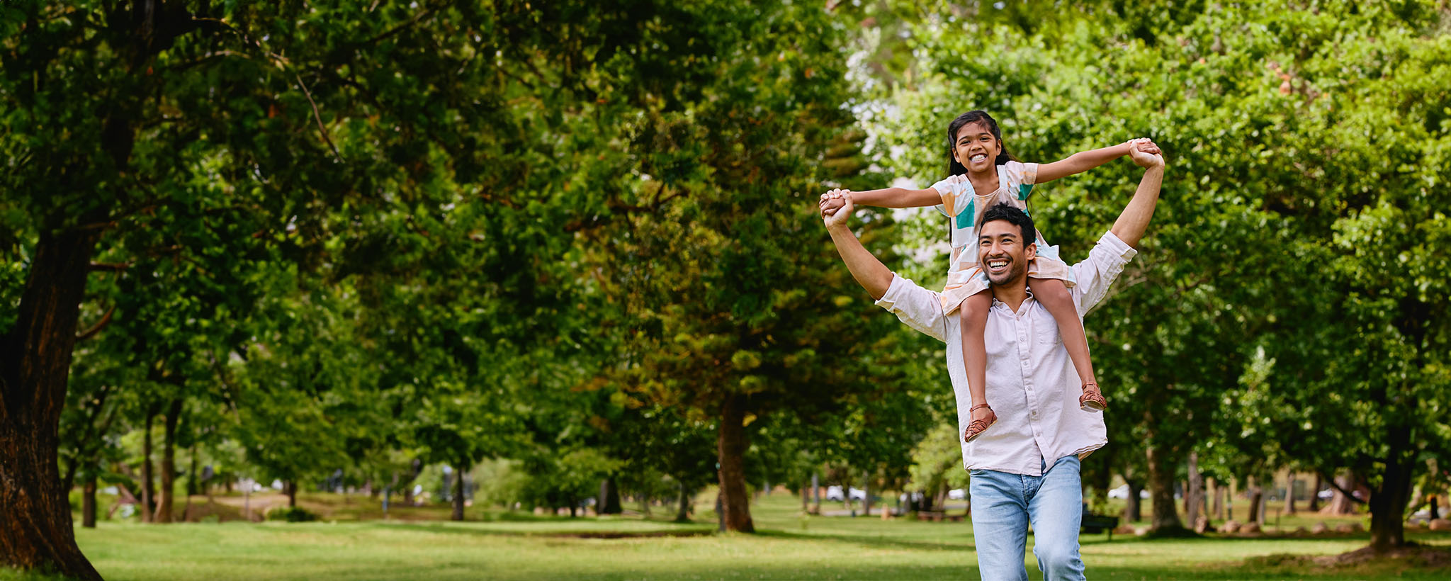 A father walks with his daughter on his shoulders in the park. 