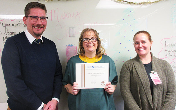 two members of faculty stand on either side of an Inside/Out program graduate proudly displaying her college readiness certificate