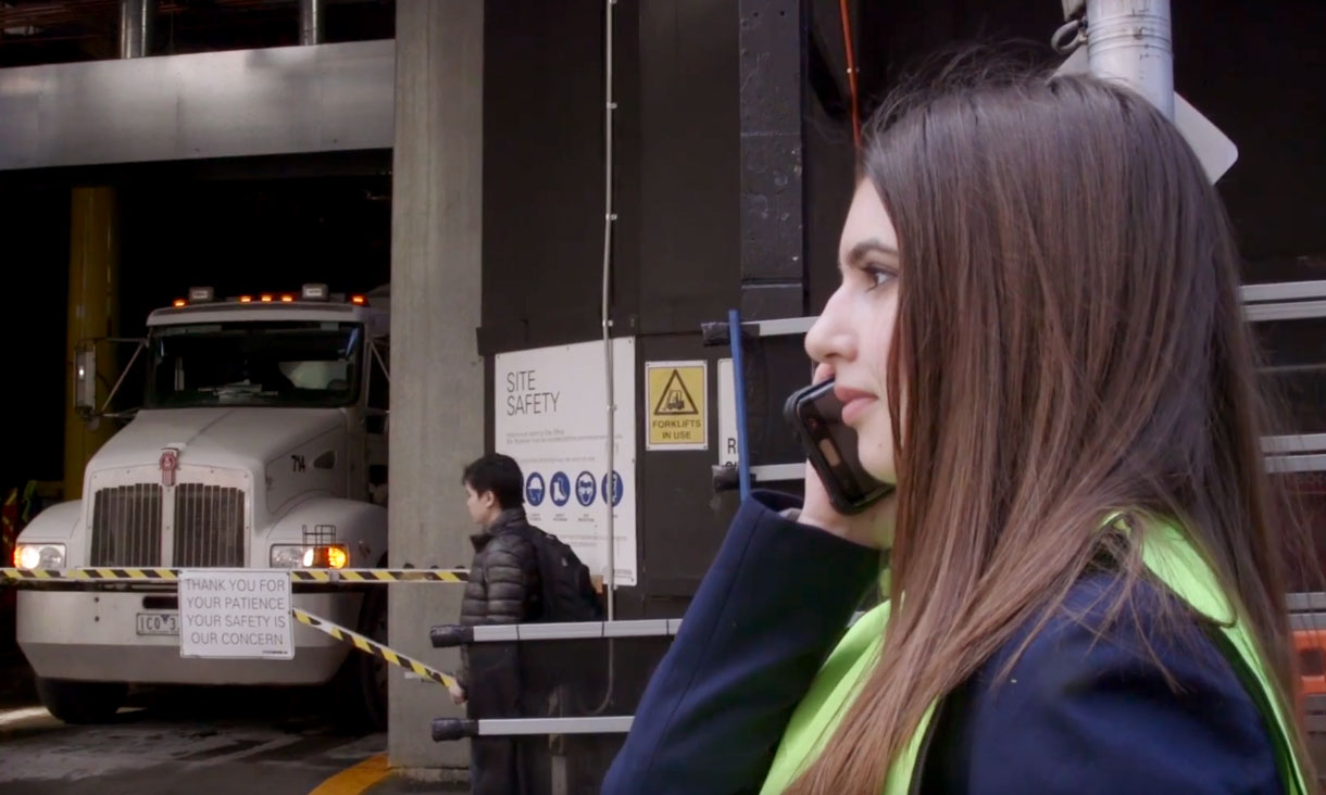 Naomi talking on her phone wearing a high-vis vest on a construction site