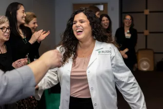 A Doctor of Nursing Practice graduate wears a white coat and smiles as other students and faculty applaud during her pinning ceremony.