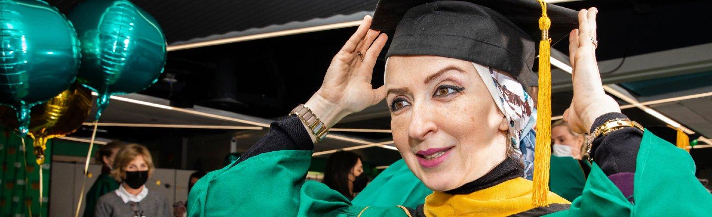 A woman wearing academic regalia adjusts her mortarboard