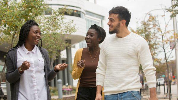 Three students talk and laugh together while walking outside