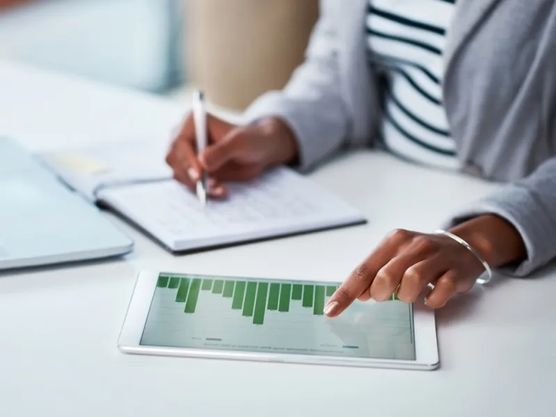 Person taking notes while viewing a graph on a tablet