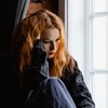 woman with Seasonal Affective Disorder is sitting on a window sill with an upset look on her face and her hand on her head