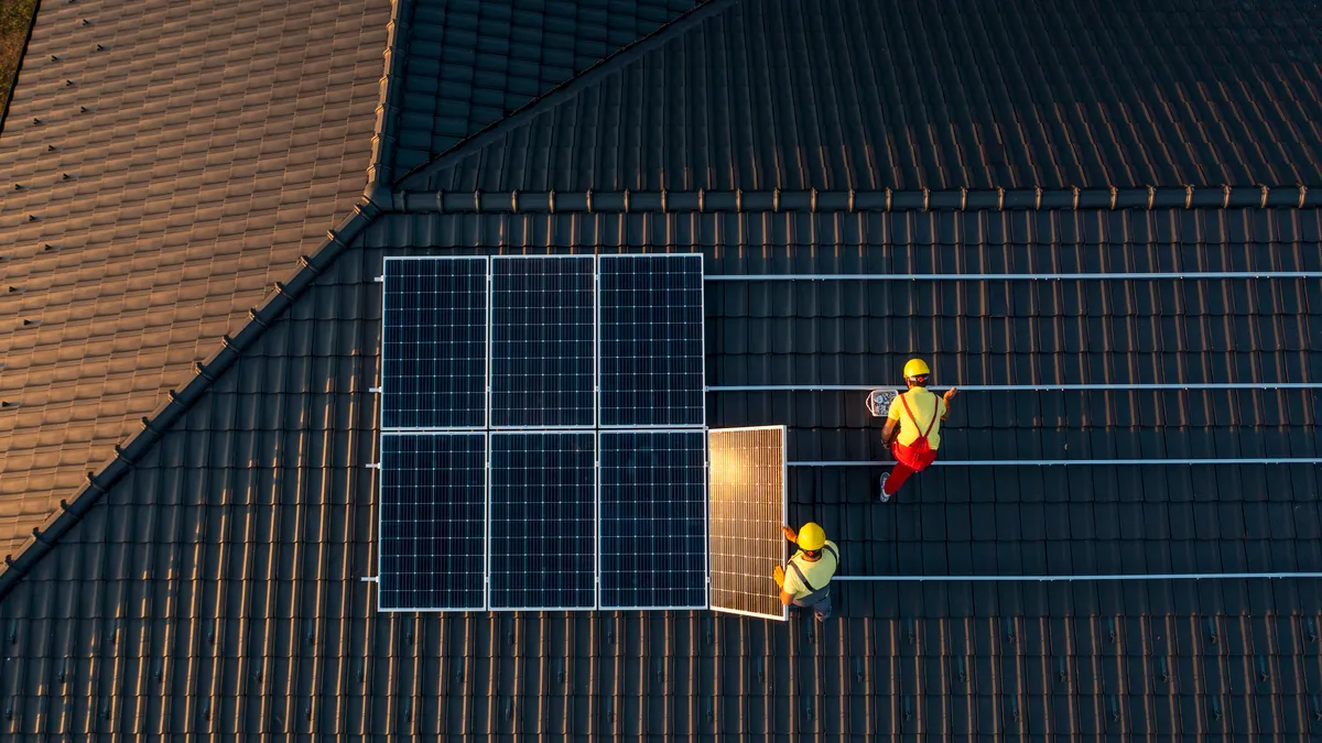 Workers install solar panels on a roof.