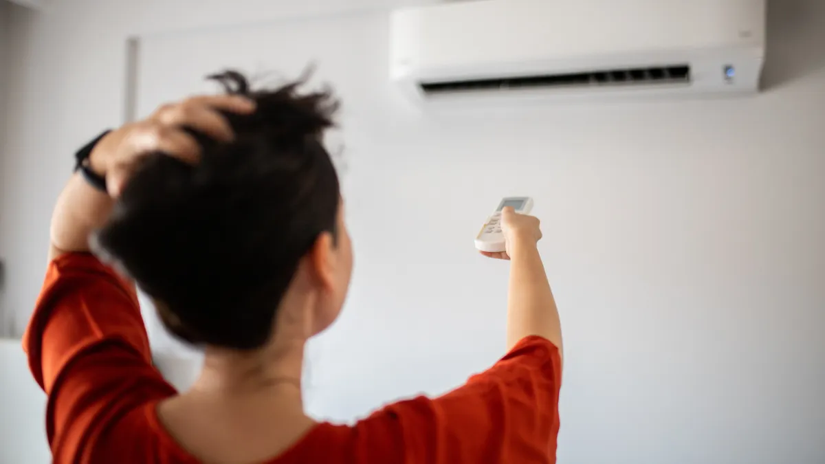 The back of a person who is pointing a remote at a wall-mounted air conditioner.