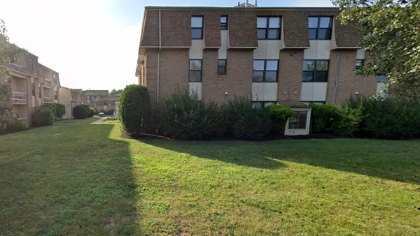 A three-story beige building surrounded by green grass.