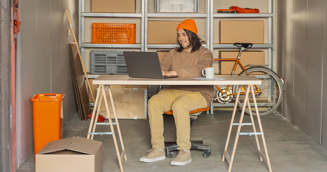 Mann sitzt in einer Garage und arbeitet an seinem Laptop