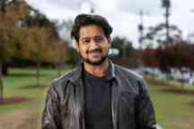 Male student wearing leather jacket stands outside smiling to camera