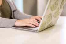 Hands typing on a laptop with a green print cover