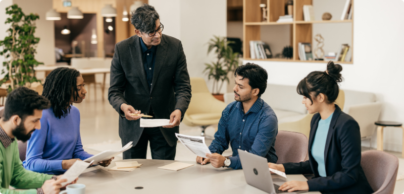 A photograph of business partners listen to a colleague present ideas on an easel.