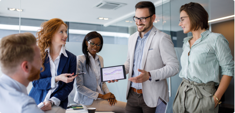 A photograph of business partners listen to a colleague present ideas on an easel.