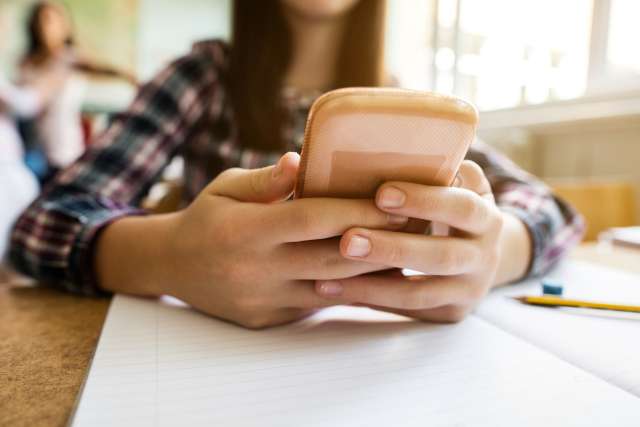 A girl holds a cellphone while sitting in a classroom.