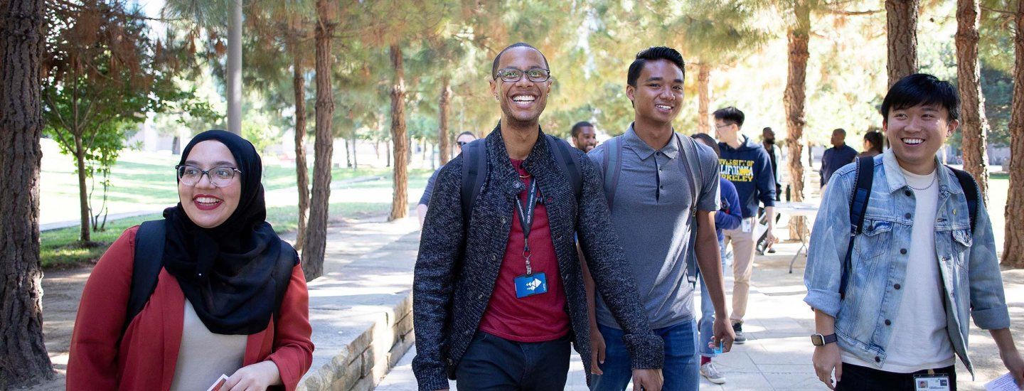 Four students in the graduate division walk along Koret Quad on a sunny day while sharing a joke