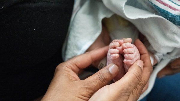 A pair of hands hold a newborn baby's feet.