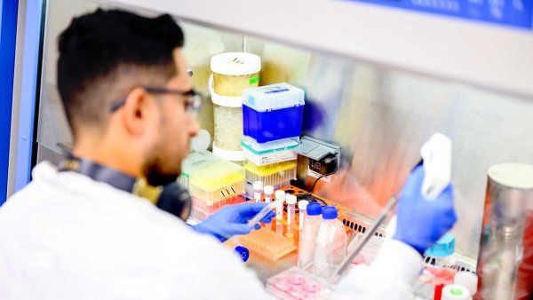 A postdoctoral student named Oscar Campos wears a lab coat as he conducts scientific research in a lab.