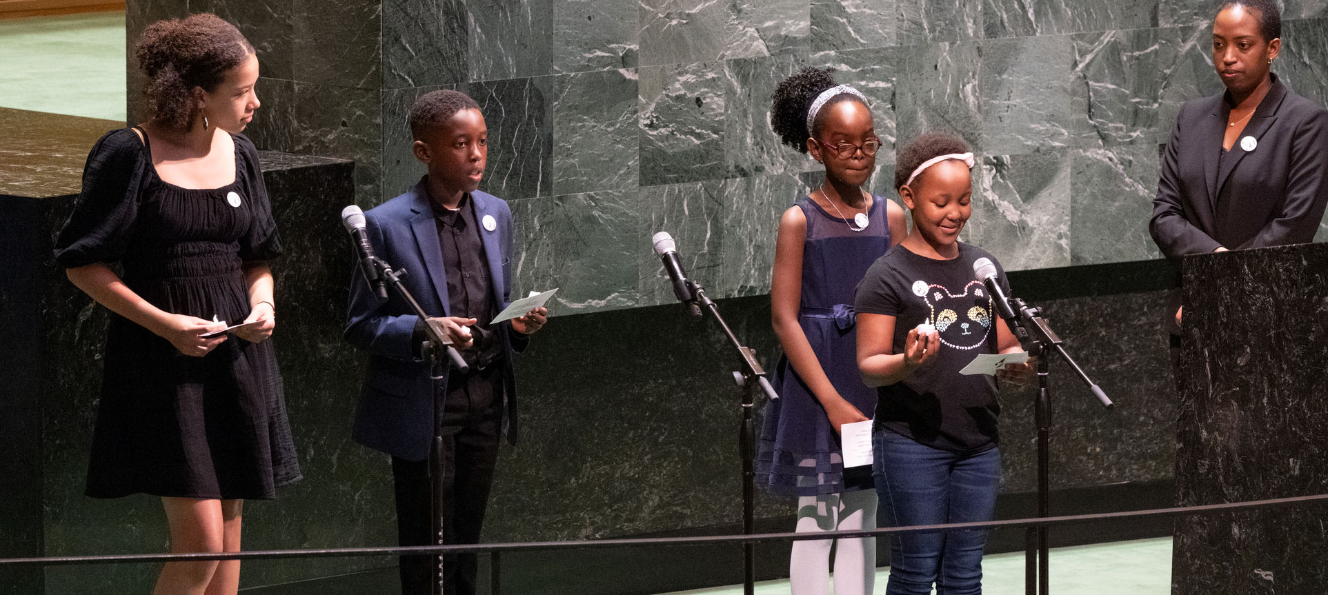 Photo of a woman and 4 children standing at the podium in the GA hall as one of them speaks