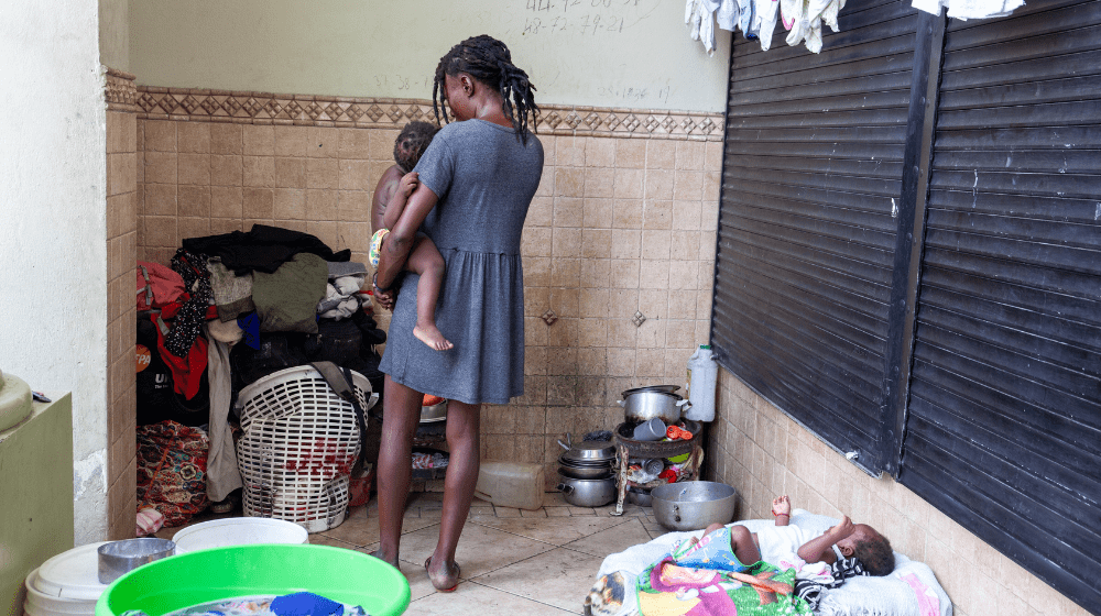 Une femme déplacée, vêtue d’une robe bleue, tient un de ses enfants dans ses bras.