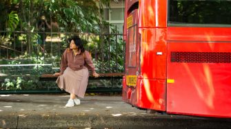 A student sitting at a bus stop on High Street outside Kensington Campus