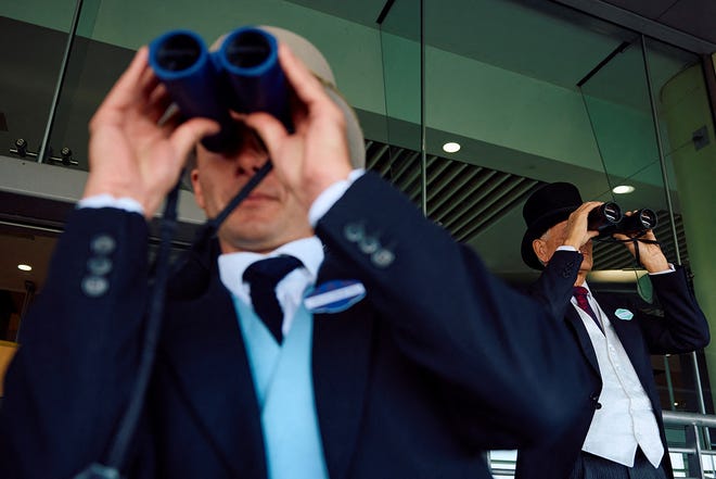 Racegoers watch a race with binoculars on the first day of the Royal Ascot horse racing meeting, in Ascot, west of London, on June 18, 2024.