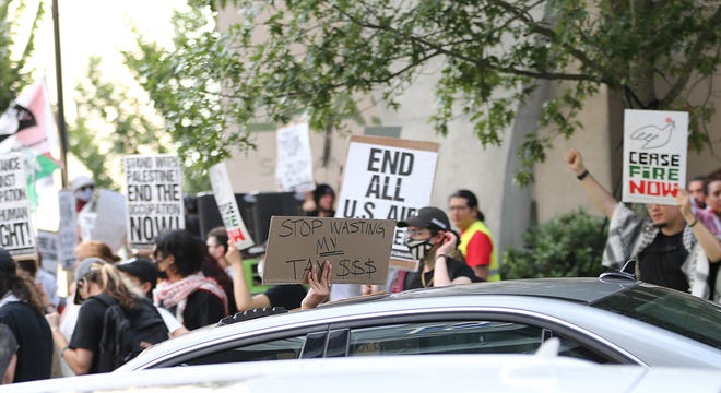 A passerby in a car holds a sign up through the sunroof as they pass a pro-Palestine rally on Spring Street, just blocks from the CNN Presidential Debate between President Joe Biden and former President Donald Trump held at CNN's studios in Atlanta.