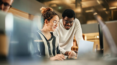 Two colleagues using laptop to discuss work project at office