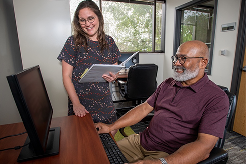 Man sits at computer with woman standing over his shoulder